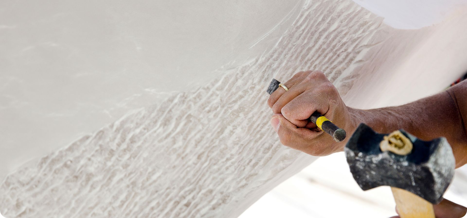 eine Hand hält einen Meißel und klopft mit einem Hammer um einen Stein zu formen